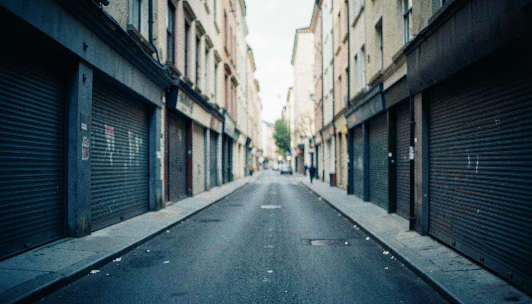 A quiet city street with closed shopfronts during daytime, muted grey and beige tones