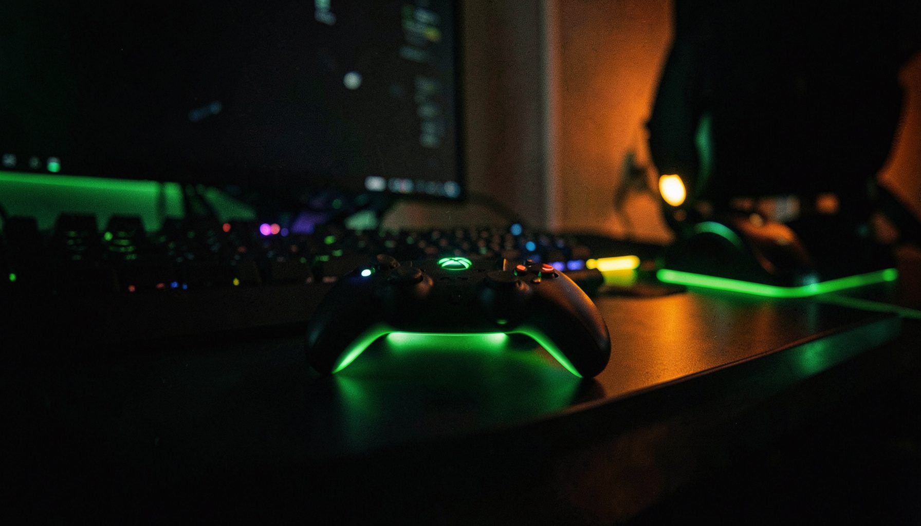 A dark gaming setup with a glowing Xbox controller resting on a desk, neon green accents against deep charcoal shadows